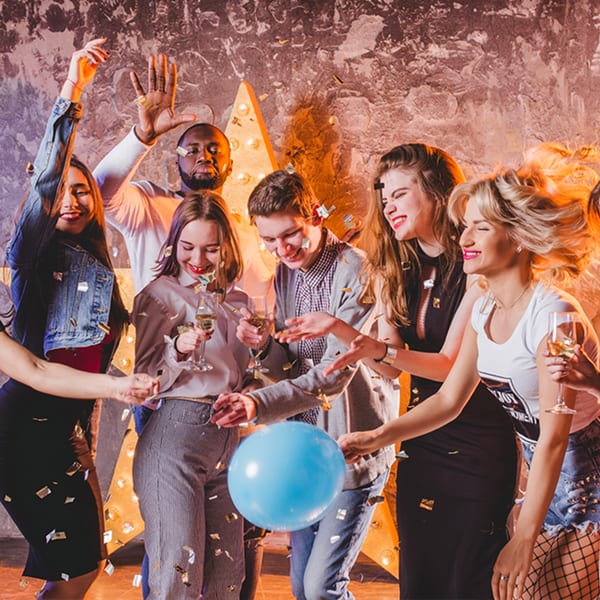 Diverse group of friends celebrating with confetti, drinks, and a blue balloon at a party.