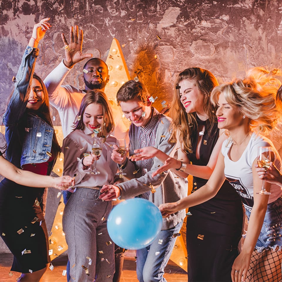 Diverse group of friends celebrating with confetti, drinks, and a blue balloon at a party.