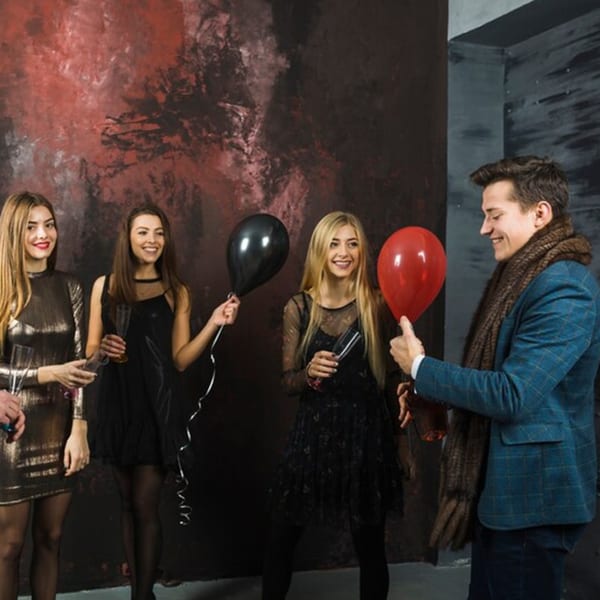 Four young adults, three women and one man, holding balloons and drinks at a party.