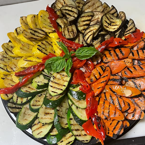 A platter of grilled vegetables including zucchini, yellow squash, eggplant, carrots, and red peppers.