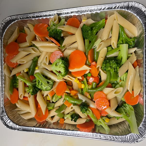 Penne pasta with mixed vegetables including broccoli, carrots, and green beans in a foil tray.